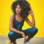 African American woman in blue outfit posing on a yellow background.