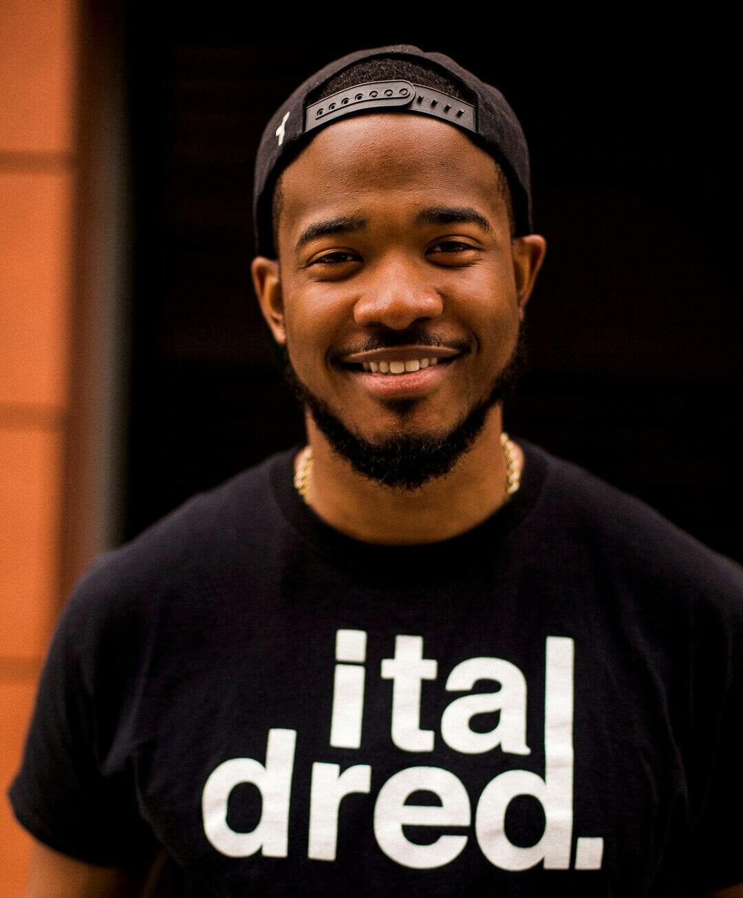 Portrait of a smiling man wearing a black t-shirt and cap outdoors.
